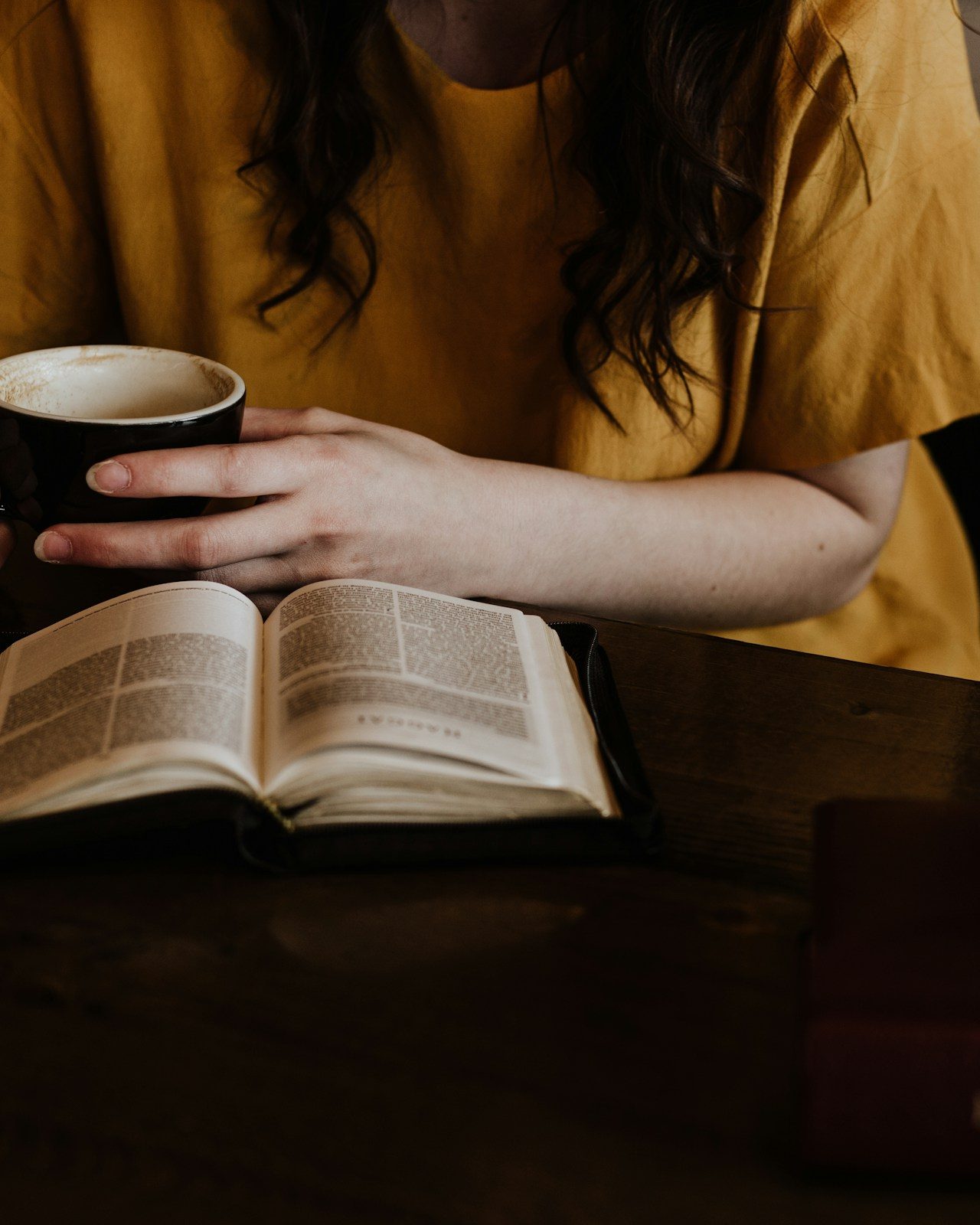 A woman holding a mug with both hands over an open Bible